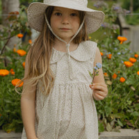 Elma Poppy Sunhat in Haru Blossom Iris, featuring tiny purple blossoms scattered across soft white Japanese-milled cotton, an adjustable crown tie and under-chin tie with toggle.
