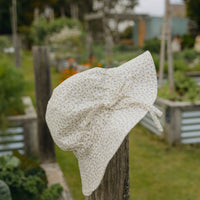Elma Poppy Sunhat in Haru Blossom Iris, featuring tiny purple blossoms scattered across soft white Japanese-milled cotton, an adjustable crown tie and under-chin tie with toggle.