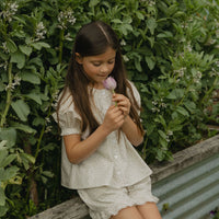 Elma Delphi Blouse in Haru Blossom Iris, featuring delicate purple florals on white Japanese-milled cotton, a shirred neckline, puff sleeves with elasticated cuffs and picot lace trim.