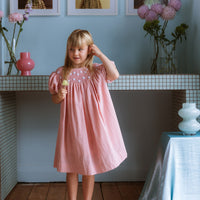 Pink cotton gingham girls’ Celeste Dress, hand‑smocked and embroidered, and puff sleeves from Elma.
