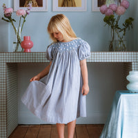 Celeste Dress in blue gingham, hand‑smocked and embroidered with petite daisies. Puff sleeves, button‑back and fully lined cotton.