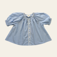 Elma Delphi Blouse in Cottage Blue Gingham, featuring soft blue and white cotton gingham, a shirred neckline, puff sleeves, elasticated cuffs and picot lace trim.