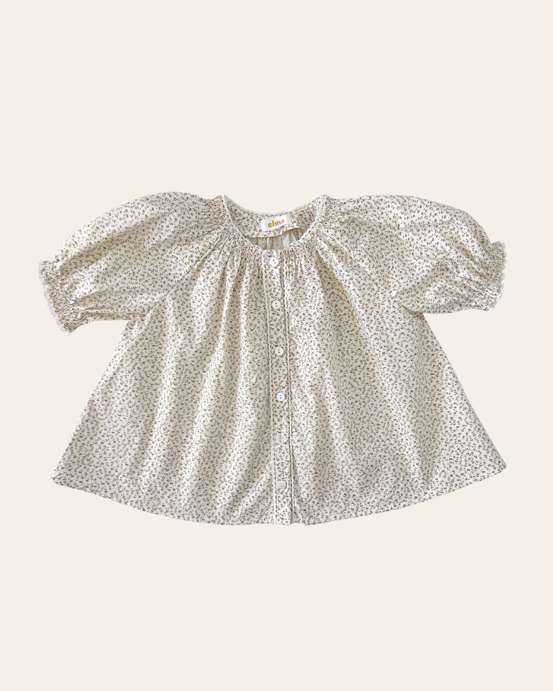 Elma Delphi Blouse in Haru Blossom Iris, featuring delicate purple florals on white Japanese-milled cotton, a shirred neckline, puff sleeves with elasticated cuffs and picot lace trim.