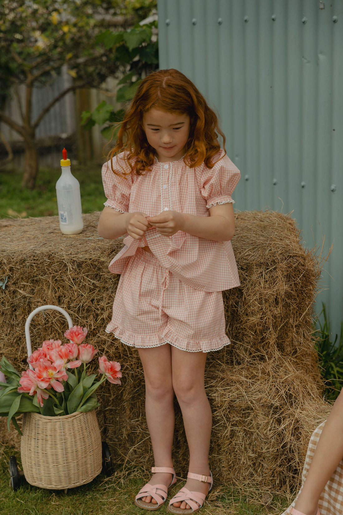Elma Lilia Shorts in pink and white Sweet Pea Gingham, featuring an elasticated drawstring waistband, side pockets and ruffled hems with delicate white picot lace trim.