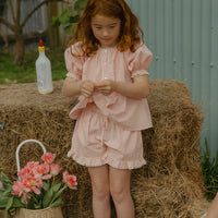 Elma Lilia Shorts in pink and white Sweet Pea Gingham, featuring an elasticated drawstring waistband, side pockets and ruffled hems with delicate white picot lace trim.