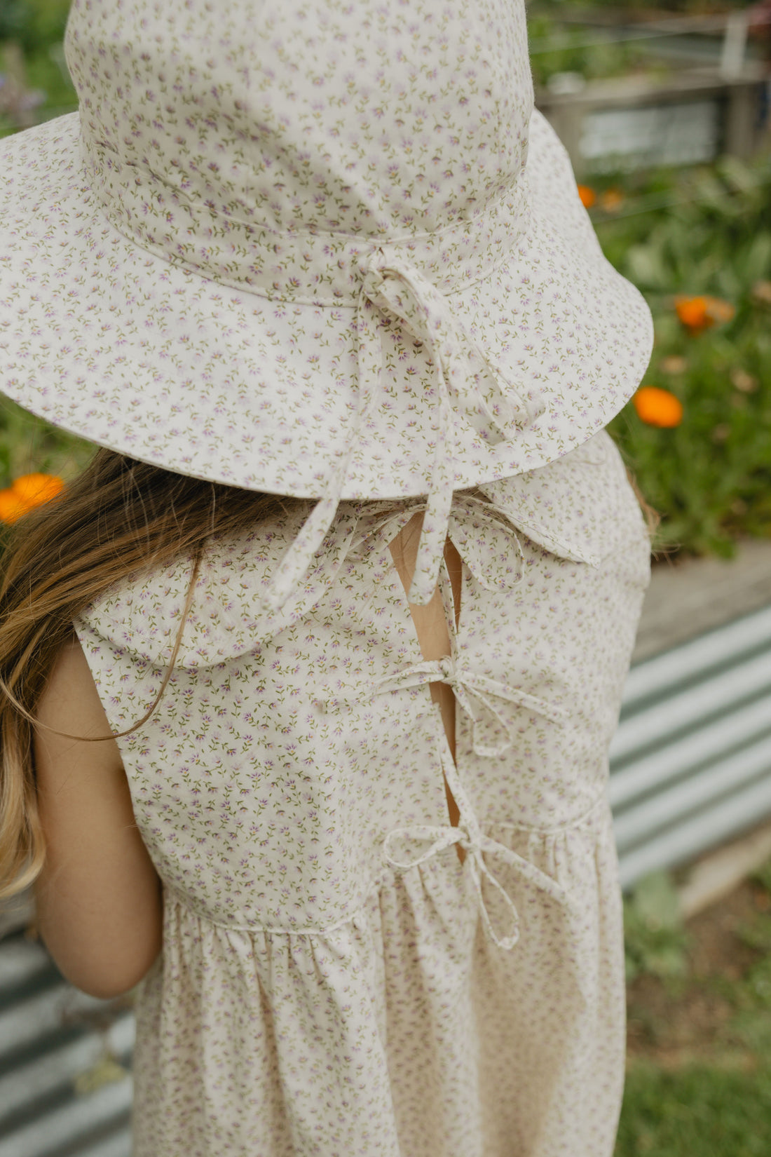 Elma Poppy Sunhat in Haru Blossom Iris, featuring tiny purple blossoms scattered across soft white Japanese-milled cotton, an adjustable crown tie and under-chin tie with toggle.