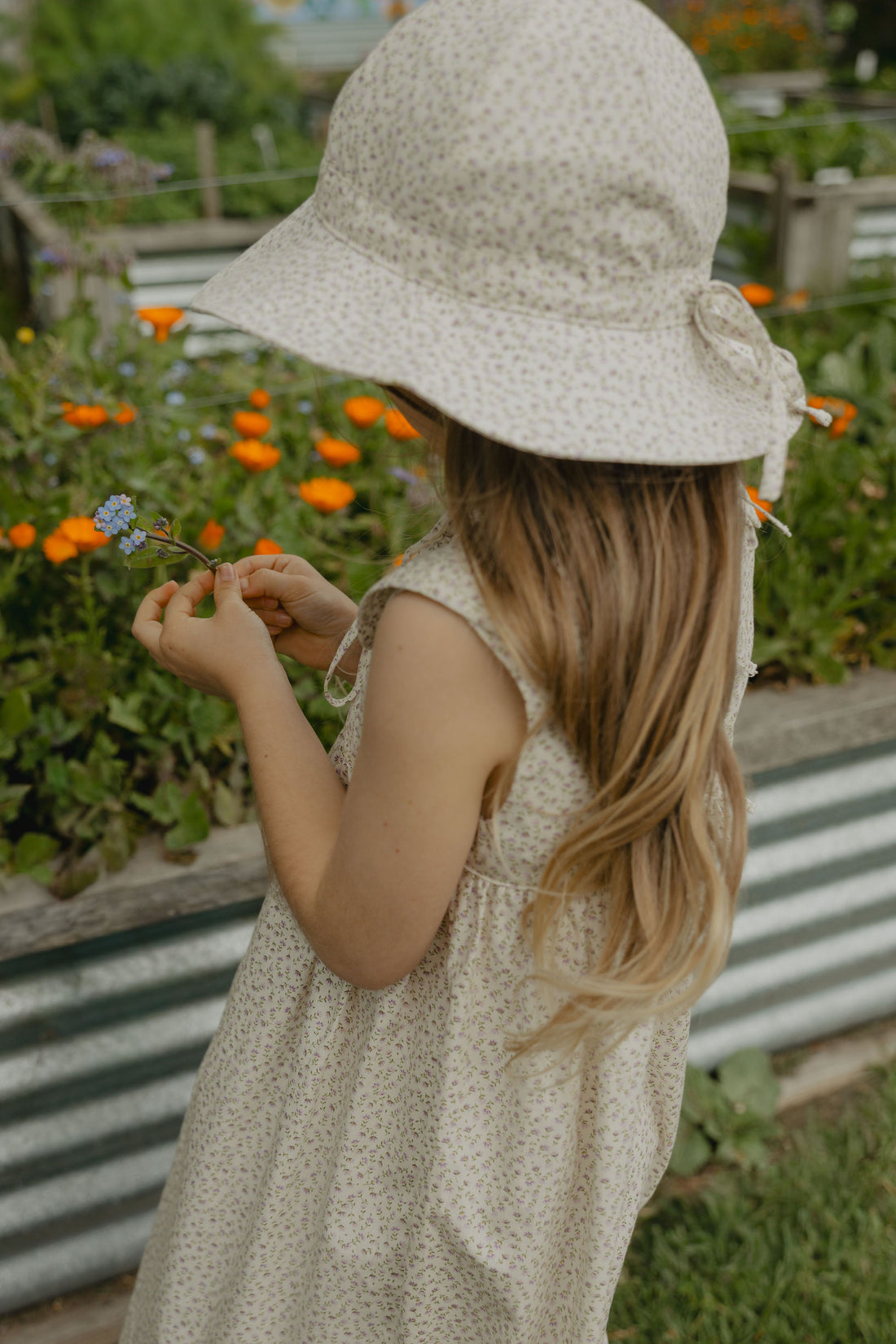 Elma Poppy Sunhat in Haru Blossom Iris, featuring tiny purple blossoms scattered across soft white Japanese-milled cotton, an adjustable crown tie and under-chin tie with toggle.