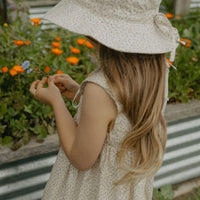 Elma Poppy Sunhat in Haru Blossom Iris, featuring tiny purple blossoms scattered across soft white Japanese-milled cotton, an adjustable crown tie and under-chin tie with toggle.