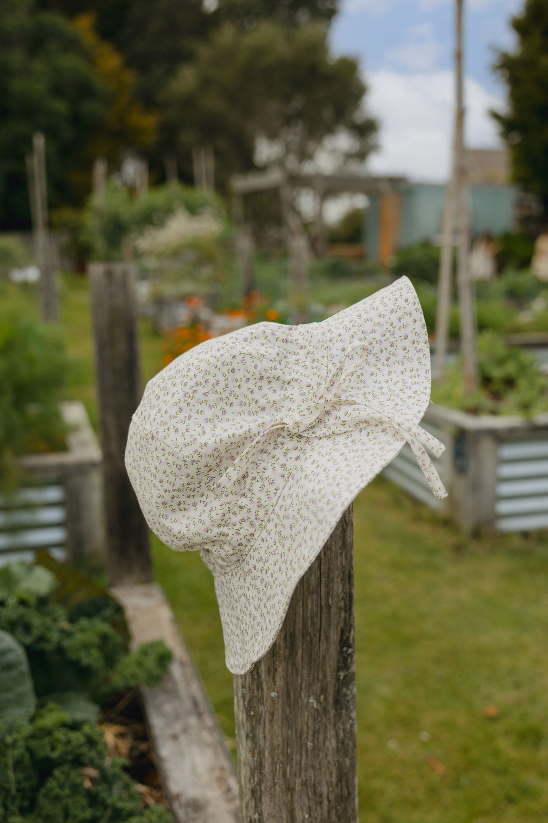 Elma Poppy Sunhat in Haru Blossom Iris, featuring tiny purple blossoms scattered across soft white Japanese-milled cotton, an adjustable crown tie and under-chin tie with toggle.