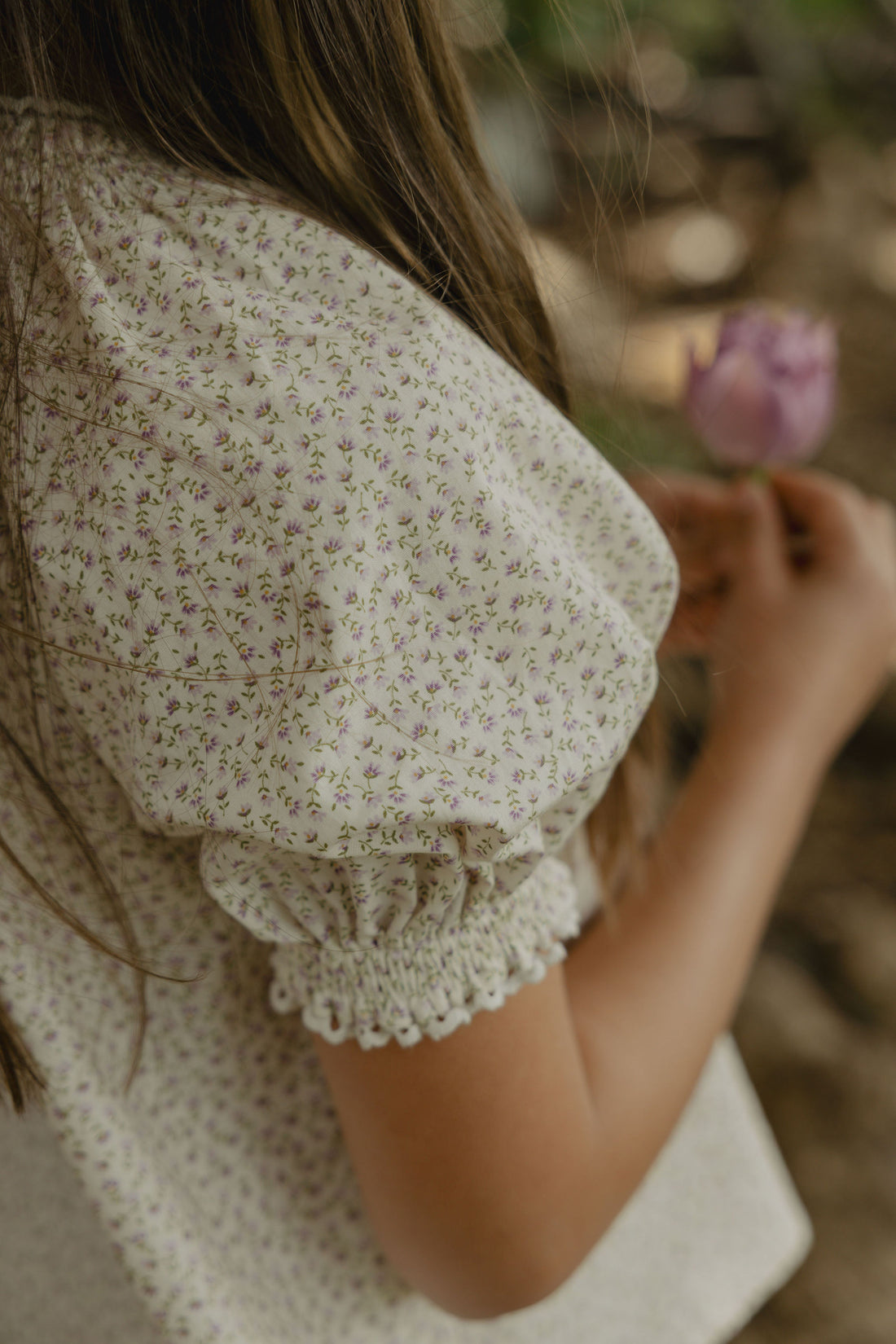 Elma Delphi Blouse in Haru Blossom Iris, featuring delicate purple florals on white Japanese-milled cotton, a shirred neckline, puff sleeves with elasticated cuffs and picot lace trim.