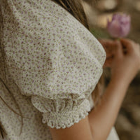 Elma Delphi Blouse in Haru Blossom Iris, featuring delicate purple florals on white Japanese-milled cotton, a shirred neckline, puff sleeves with elasticated cuffs and picot lace trim.
