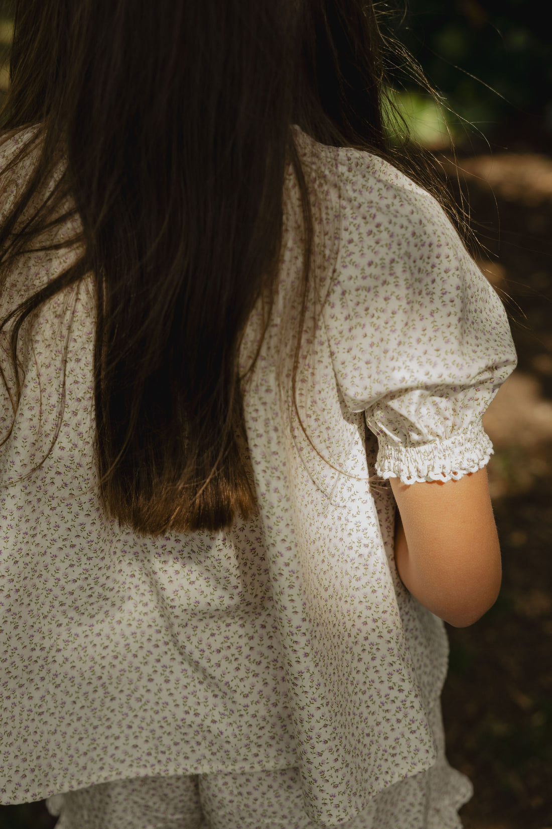 Elma Delphi Blouse in Haru Blossom Iris, featuring delicate purple florals on white Japanese-milled cotton, a shirred neckline, puff sleeves with elasticated cuffs and picot lace trim.