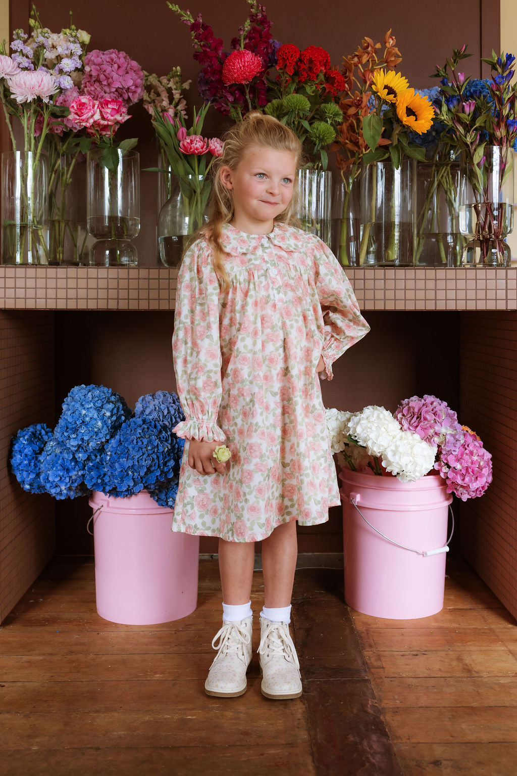 Girl wearing the Elodie Dress in Liberty Willmotts Roses floral print in pink and cream tones, with scalloped Peter Pan collar puff long sleeves.
