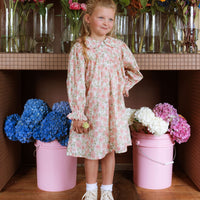 Girl wearing the Elodie Dress in Liberty Willmotts Roses floral print in pink and cream tones, with scalloped Peter Pan collar puff long sleeves.