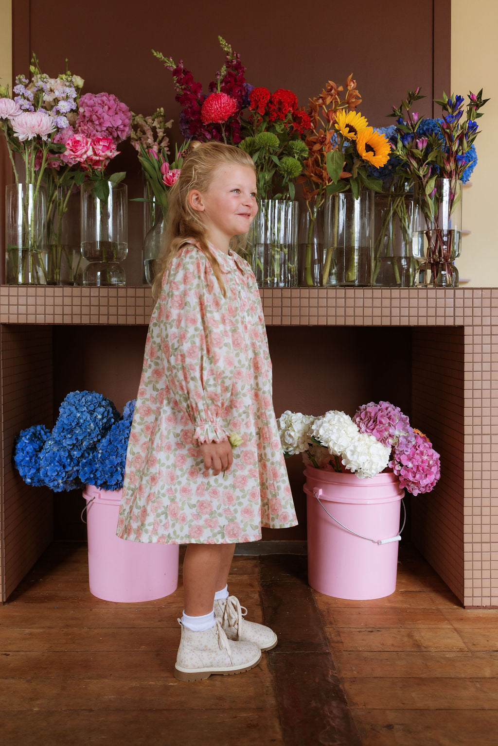 Girl wearing the Elodie Dress in Liberty Willmotts Roses floral print in pink and cream tones, with scalloped Peter Pan collar puff long sleeves.