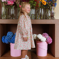 Girl wearing the Elodie Dress in Liberty Willmotts Roses floral print in pink and cream tones, with scalloped Peter Pan collar puff long sleeves.