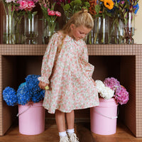 Girl wearing the Elodie Dress in Liberty Willmotts Roses floral print in pink and cream tones, with scalloped Peter Pan collar puff long sleeves.