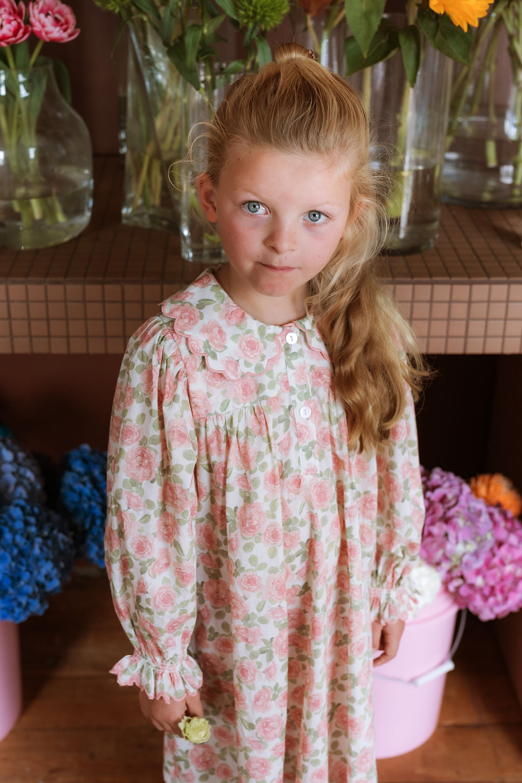 Girl wearing the Elodie Dress in Liberty Willmotts Roses floral print in pink and cream tones, with scalloped Peter Pan collar puff long sleeves.