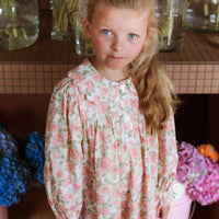 Girl wearing the Elodie Dress in Liberty Willmotts Roses floral print in pink and cream tones, with scalloped Peter Pan collar puff long sleeves.