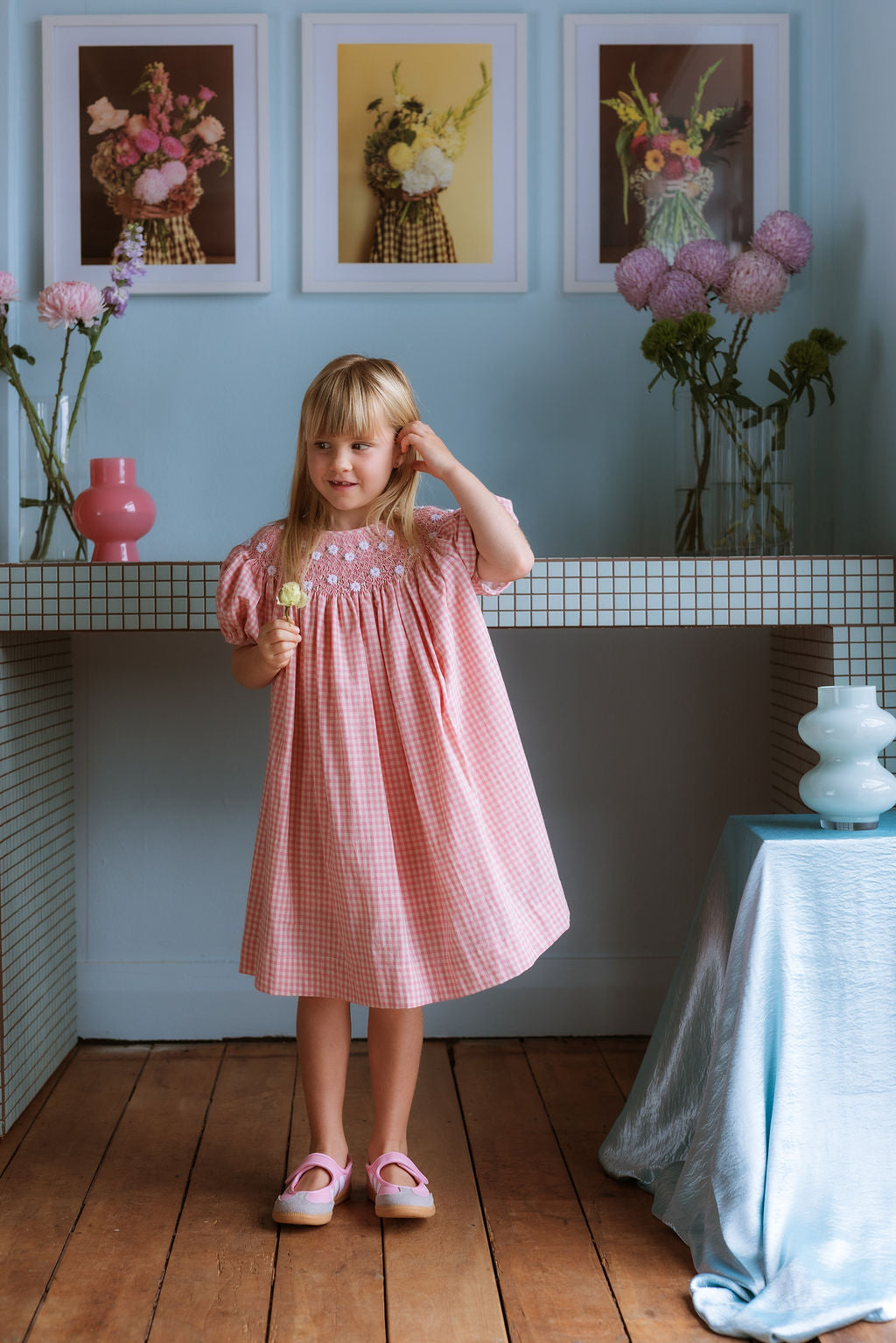 Pink cotton gingham girls’ Celeste Dress, hand‑smocked and embroidered, and puff sleeves from Elma.