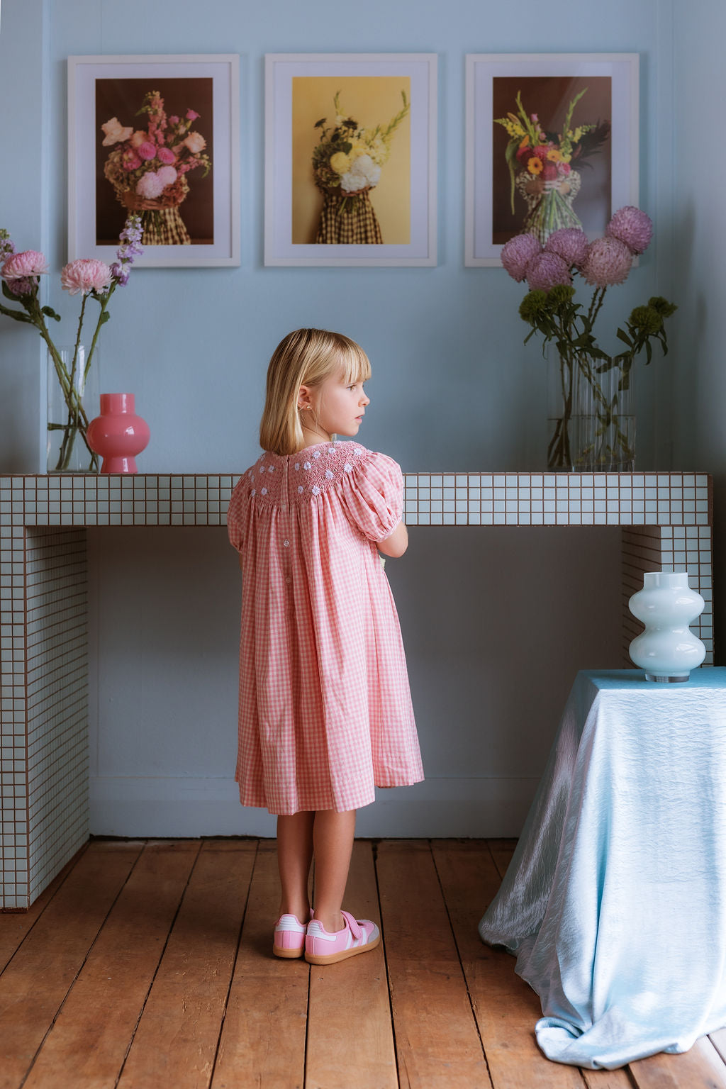 Pink cotton gingham girls’ Celeste Dress, hand‑smocked and embroidered, and puff sleeves from Elma.