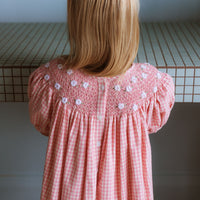 Pink cotton gingham girls’ Celeste Dress, hand‑smocked and embroidered, and puff sleeves from Elma.
