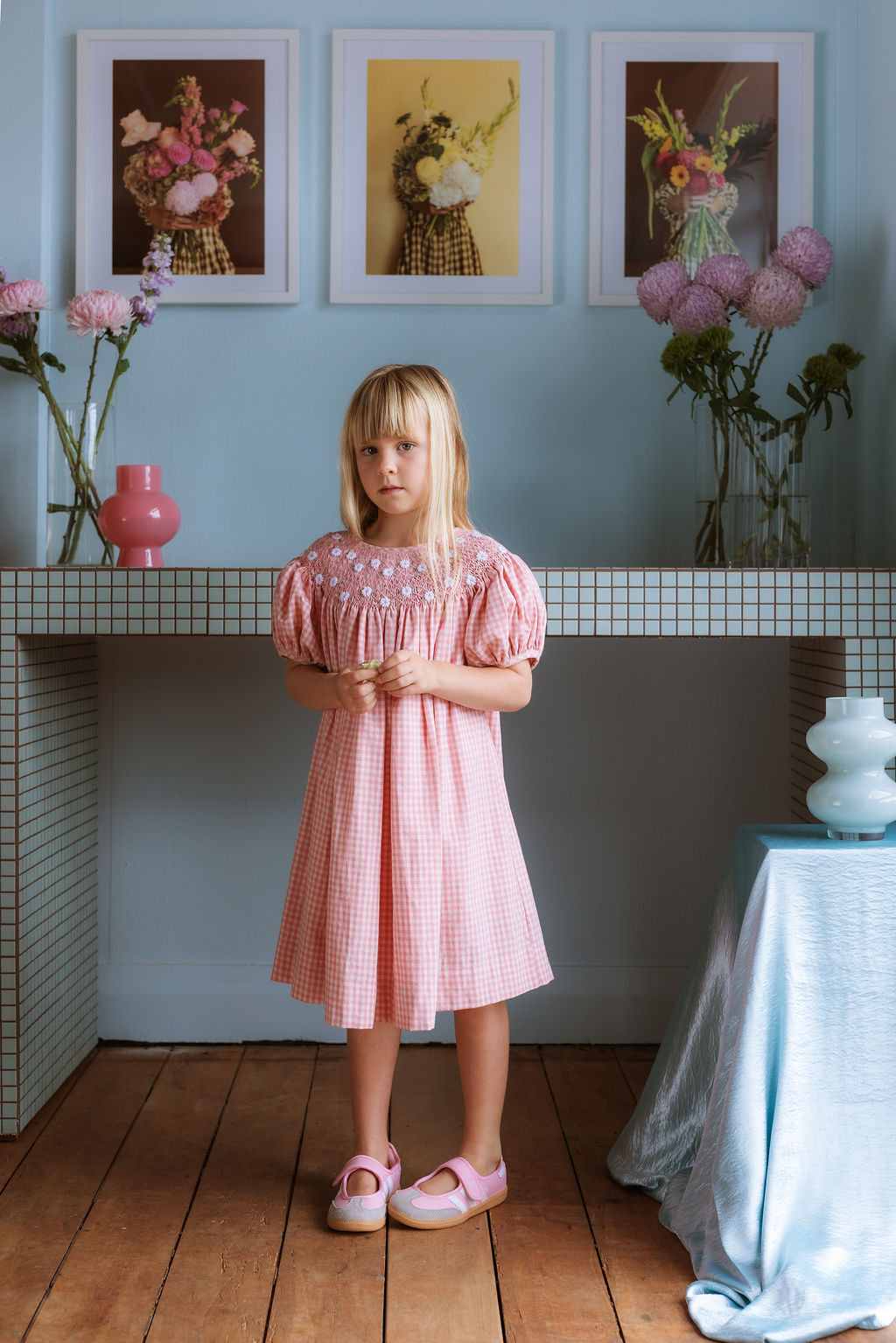 Pink cotton gingham girls’ Celeste Dress, hand‑smocked and embroidered, and puff sleeves from Elma.