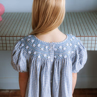 Celeste Dress in blue gingham, hand‑smocked and embroidered with petite daisies. Puff sleeves, button‑back and fully lined cotton.