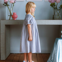 Celeste Dress in blue gingham, hand‑smocked and embroidered with petite daisies. Puff sleeves, button‑back and fully lined cotton.
