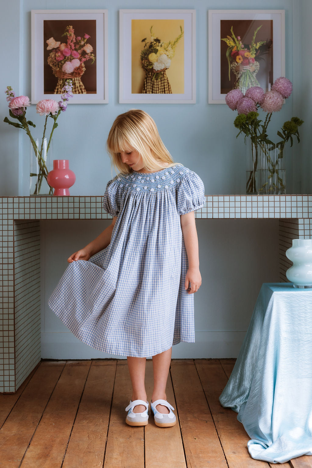Celeste Dress in blue gingham, hand‑smocked and embroidered with petite daisies. Puff sleeves, button‑back and fully lined cotton.