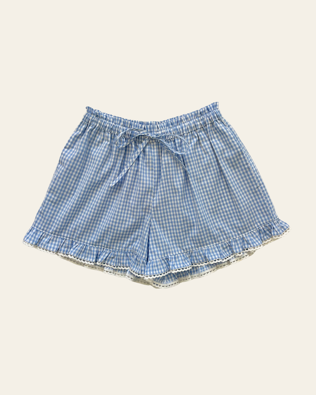 Elma Lilia Shorts in blue and white Cottage Blue Gingham, featuring an elasticated drawstring waistband, side pockets and ruffled hems with delicate white picot lace trim.