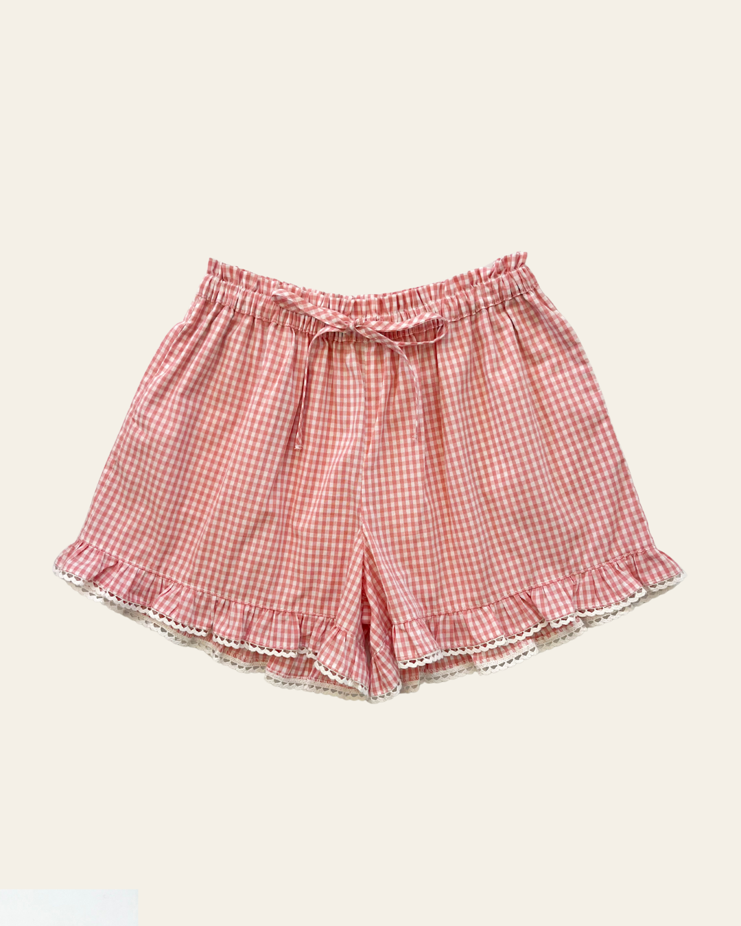 Elma Lilia Shorts in pink and white Sweet Pea Gingham, featuring an elasticated drawstring waistband, side pockets and ruffled hems with delicate white picot lace trim.