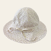 Elma Poppy Sunhat in Haru Blossom Iris, featuring tiny purple blossoms scattered across soft white Japanese-milled cotton, an adjustable crown tie and under-chin tie with toggle.