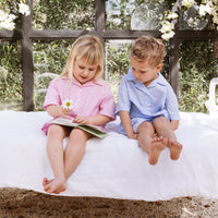 Girl and boy sitting on a bed reading a childrens story. One is wearing a pink stripe shirt and shorts set. The other is wearing a blue stripe shirt and shorts set.