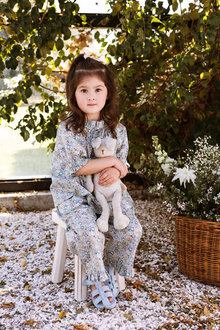Girl sitting on a stool holding onto her bunny. She wears a Liberty floral top, matching pants and blue sandals.